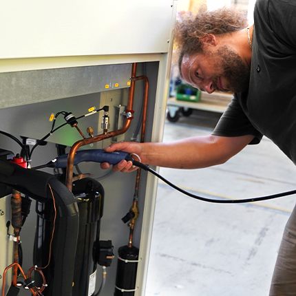 Ein Mitarbeiter aus der Abteilung Qualität arbeitet an einer Wärmepumpe. Die Maschine ist geöffnet und wird von ihm überprüft. 