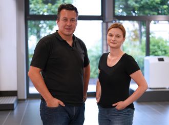 Die beiden Ausbildungsleiter Helmut Lauterbach und Melanie Bloch-Schönthier stehen nebeneinander im Forum, die Hände locker in die Hosentaschen gesteckt, lächeln Sie in die Kamera.