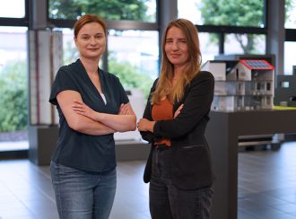 Zwei Mitarbeiterinnen der Personalabteilung sind zu sehen. Sie stehen im Forumsgebäude der Glen Dimplex Deutschland GmbH. Sie stehen nebeneinander, die Arme selbstbewusst vor der Brust verschränkt und lächeln kompetent in die Kamera.
