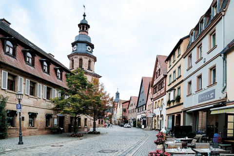 Das Bild zeigt die Innenstadt von Kulmbach. Links und rechts der Straße säumen sich ältere Gebäude. Im Hintergrund ist ein Turm zu sehen. 