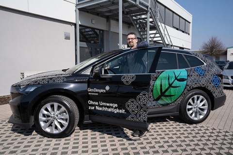 Zu sehen ist ein Mitarbeiter von Glen Dimplex Deutschland. Er steht in der geöffneten Fahrertür. Das Auto ist beschriftet mit vielen GDD-Knoten, einem grünen Blatt und dem Schriftzug "Ohne Umwege zur Nachhaltigkeit".