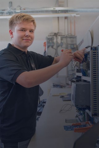 Das Bild zeigt einen jungen technischen Auszubildenden der gerade an einem Produkt arbeitet. Man sieht das technische Innenleben des Geräts.