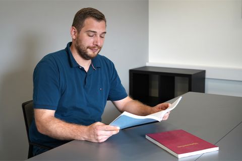 Ein junger Student sitzt an einem Tisch und liest in seiner gedruckten Version der Bachelor-Arbeit.