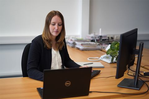 Eine junge Werksstudentin ist an ihrem Arbeitsplatz zu sehen. Sie blickt konzentriert auf ihren Laptop-Bildschirm. 