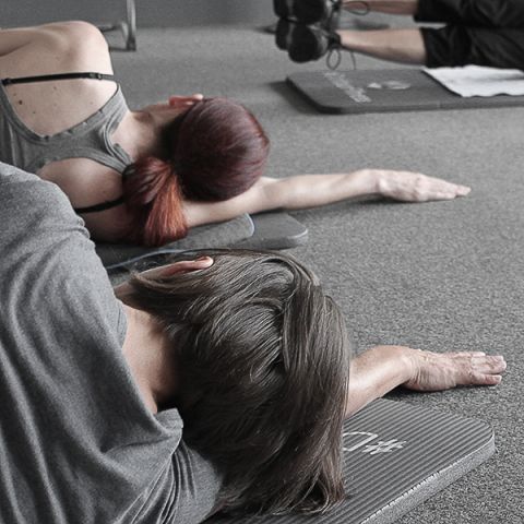 Mehrere Personen liegen auf Sportmatten und machen Yoga-Übungen.