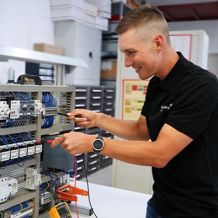 Ein junger männlicher Mitarbeiter in schwarzem Firmen-Polo-Shirt nimmt an einem Produkt Messungen vor.